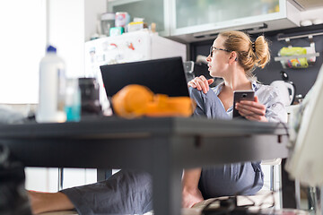 Image showing Stay at home and social distancing. Woman in her casual home clothing working remotly from kitchen dining table. Video chatting using social media with friend, family, business clients or partners