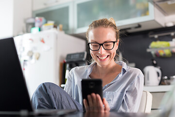 Image showing Stay at home and social distancing. Woman in her casual home clothing working remotly from kitchen dining table. Video chatting using social media with friend, family, business clients or partners