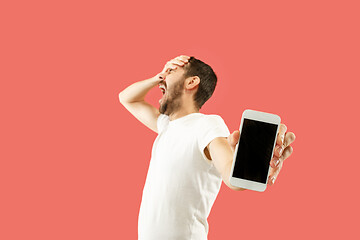 Image showing Young handsome man showing smartphone screen isolated on coral background in shock with a surprise face