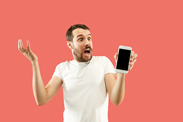 Image showing Young handsome man showing smartphone screen isolated on coral background in shock with a surprise face