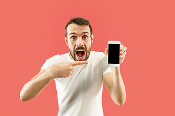 Image showing Young handsome man showing smartphone screen isolated on coral background in shock with a surprise face