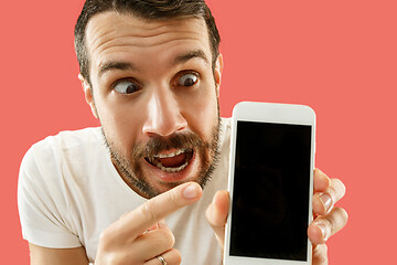Image showing Young handsome man showing smartphone screen isolated on coral background in shock with a surprise face