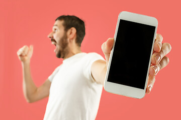 Image showing Young handsome man showing smartphone screen isolated on coral background in shock with a surprise face