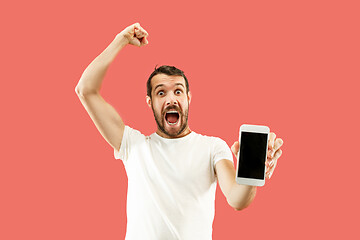 Image showing Young handsome man showing smartphone screen isolated on coral background in shock with a surprise face