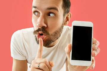 Image showing Young handsome man showing smartphone screen isolated on coral background in shock with a surprise face