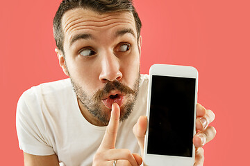 Image showing Young handsome man showing smartphone screen isolated on coral background in shock with a surprise face