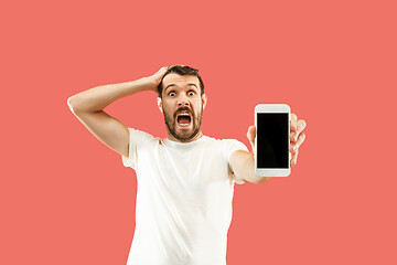 Image showing Young handsome man showing smartphone screen isolated on coral background in shock with a surprise face