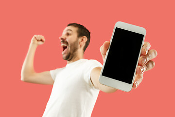 Image showing Young handsome man showing smartphone screen isolated on coral background in shock with a surprise face