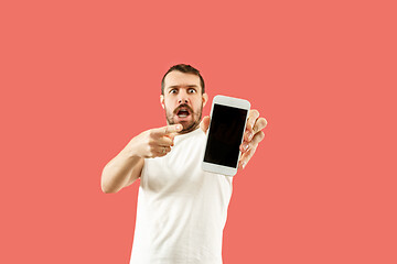 Image showing Young handsome man showing smartphone screen isolated on coral background in shock with a surprise face