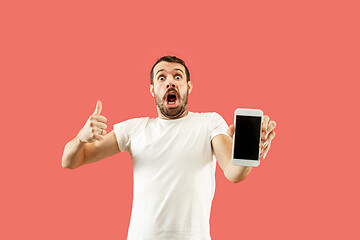 Image showing Young handsome man showing smartphone screen isolated on coral background in shock with a surprise face