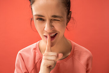 Image showing The young woman whispering a secret behind her hand over coral background