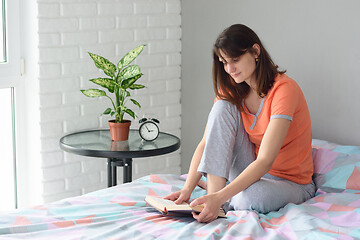 Image showing Girl sitting in bed in pajamas and reading a book