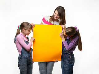 Image showing Mom and two daughters hold an orange sign in their hands and look at it