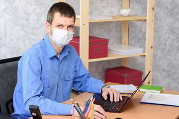 Image showing Portrait of an office worker in a medical mask at a desk