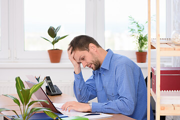 Image showing Upset office worker looking at documents clutching his head