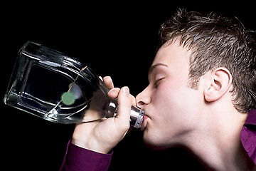 Image showing The young man drinks vodka from a bottle. Isolated on black