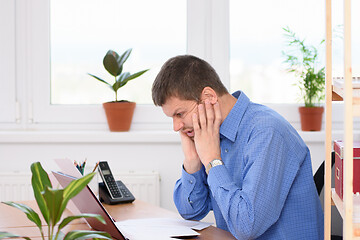 Image showing Office clerk grimacing grimacing pain on his face looking at a laptop