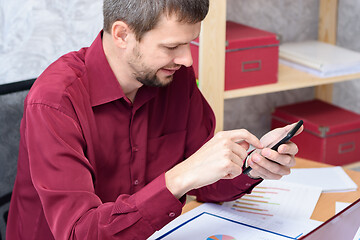 Image showing man with a smile looks at the smartphone at the desk in the office