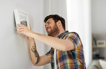 Image showing man hanging picture in frame to wall at home