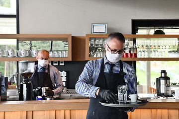 Image showing waiter in a medical protective mask serves  the coffee in restau