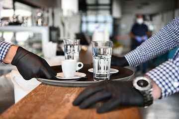 Image showing waiter in a medical protective mask serves  the coffee in restau