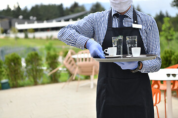 Image showing waiter in a medical protective mask serves  the coffee in restau