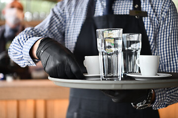 Image showing waiter in a medical protective mask serves  the coffee in restau