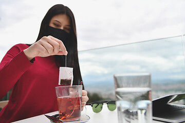 Image showing woman in restaurant drinking tea wearingmedical  face mask