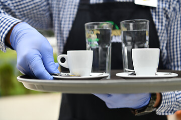 Image showing waiter in a medical protective mask serves  the coffee in restau