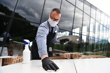 Image showing Waiter cleaning the table with Disinfectant Spray in a restauran