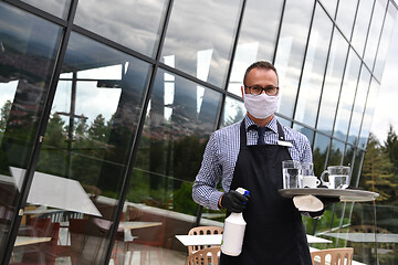 Image showing Waiter cleaning the table with Disinfectant Spray in a restauran