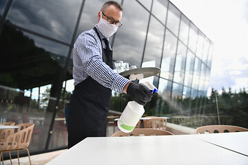 Image showing Waiter cleaning the table with Disinfectant Spray in a restauran