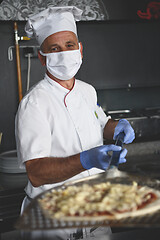 Image showing chef  with protective coronavirus face mask preparing pizza