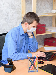 Image showing An office worker sits at a desk wearing a medical mask