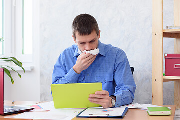 Image showing A man in the office with a tablet in his hand coughs in a napkin