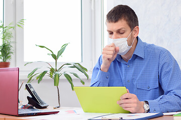 Image showing sick office worker in medical mask sits at desk