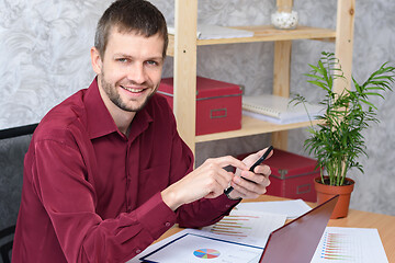 Image showing Smiling office worker corresponds on his smartphone