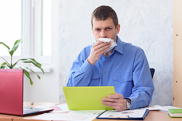 Image showing An office worker with a tablet in his hand holds a napkin at his mouth