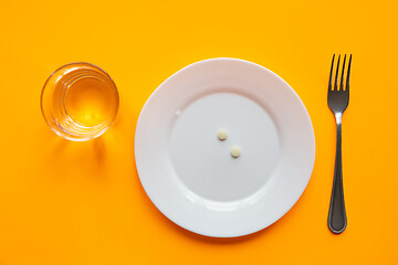 Image showing On the plate is a handful of pills, next to it is a glass of water and a fork