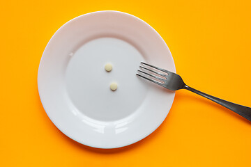 Image showing On the plate are two tablets and a fork, orange background