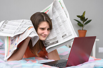 Image showing Girl put newspapers to her head and looks at the laptop screen trying to find work