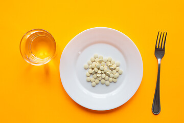 Image showing On the plate are two tablets, next to it is a glass of water and a fork