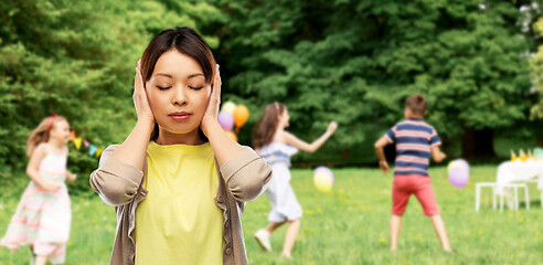 Image showing asian woman closing ears over kids party at park