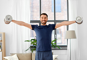 Image showing smiling man exercising with dumbbells at home