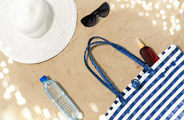 Image showing beach bag, sunscreen, sunglasses and hat on sand