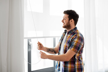 Image showing man opening roller blind on window at home