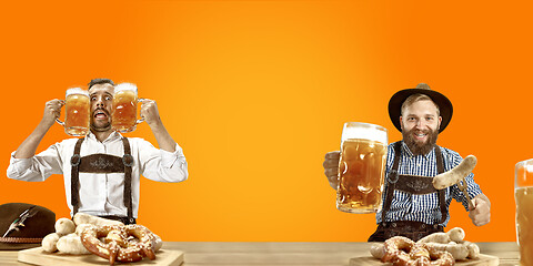 Image showing Smiling men with beer dressed in traditional Austrian or Bavarian costume holding mug of beer at pub or studio. The celebration, oktoberfest, festival