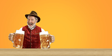 Image showing Smiling senior man with beer dressed in traditional Austrian or Bavarian costume holding mug of beer at pub or studio. The celebration, oktoberfest, festival