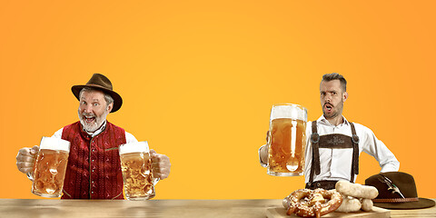 Image showing Smiling men with beer dressed in traditional Austrian or Bavarian costume holding mug of beer at pub or studio. The celebration, oktoberfest, festival