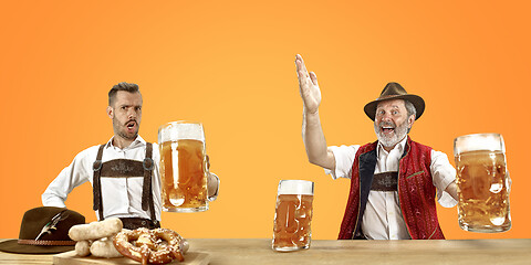 Image showing Smiling men with beer dressed in traditional Austrian or Bavarian costume holding mug of beer at pub or studio. The celebration, oktoberfest, festival